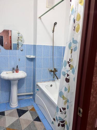 La salle de bains est pourvue de carrelage bleu, d'une baignoire et d'un lavabo. dans l'établissement Апартаменты с 2 спальнями, à Atyraū