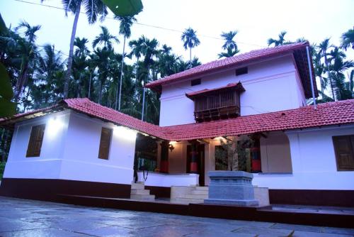 uma casa branca com um telhado vermelho e palmeiras em Kaanayi heritage home em Kokkānisseri