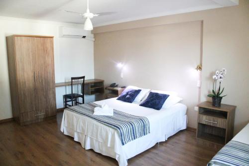 a bedroom with a bed and a desk and a chair at Hotel Águas Virtuosas in Lambari