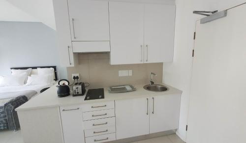 a white kitchen with a sink and a bed at iTowers Studio-Suite in Gaborone