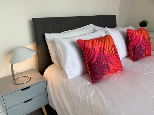uma cama com almofadas vermelhas e brancas e uma mesa de cabeceira em Chertsey - Beautiful Modern 2 Bedroom Apartment em Chertsey
