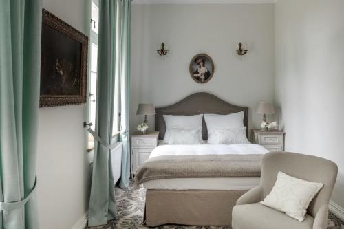 a white bedroom with a bed and a chair at Pałac Kamieniec in Polanica-Zdrój
