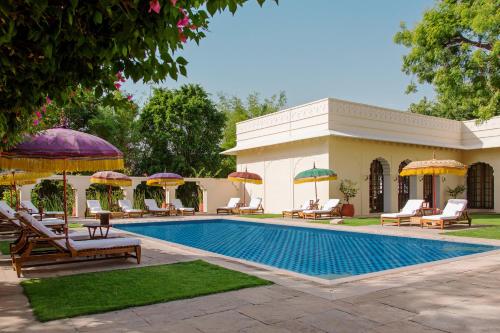 The Oberoi Vanyavilas Wildlife Resort, Ranthambhore في ساواي مادهوبور: مسبح مع كراسي ومظلات بجوار منزل