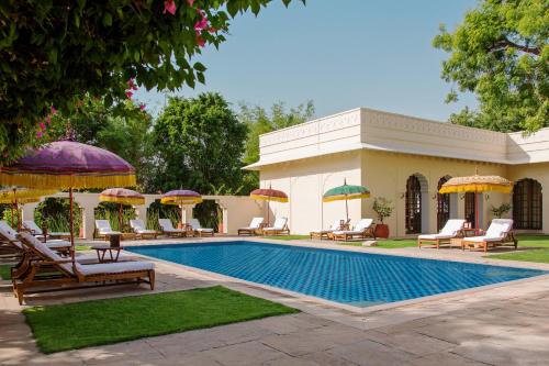 a pool with chairs and umbrellas next to a house at The Oberoi Vanyavilas Wildlife Resort, Ranthambhore in Sawāi Mādhopur