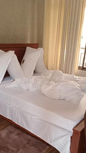 1 cama no hecha con sábanas y almohadas blancas en Amarula Tree Hotel, en Mikumi