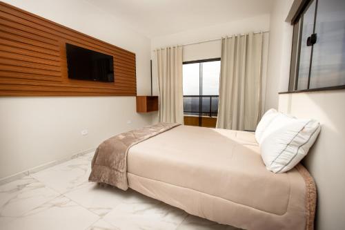 um quarto com uma cama e uma televisão na parede em ECOLETRAS APART - HOTEL - SÃO THOMÉ DAS LETRAS Mg em São Tomé das Letras