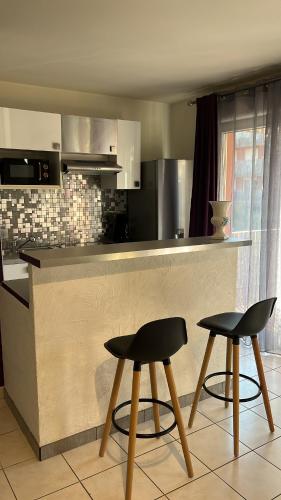 une cuisine avec deux tabourets noirs devant un comptoir dans l'établissement Superbe T2 à Balaruc les Bains, à Balaruc-les-Bains