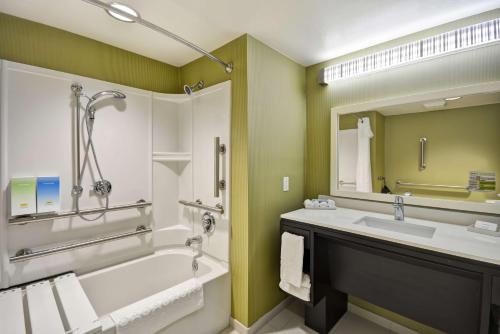 a bathroom with a tub and a sink and a mirror at Home2 Suites By Hilton Oswego in Oswego
