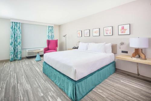 une chambre d'hôtel avec un lit et une chaise rose dans l'établissement Hilton Garden Inn Surprise Phoenix, à Surprise