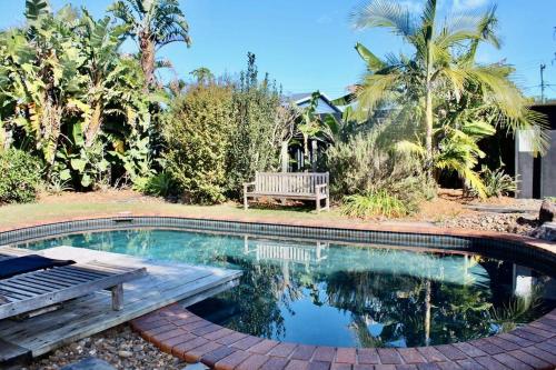 a swimming pool with a wooden bench and a bench at Caba Beach Casa in Cabarita Beach