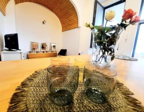 a table with two glasses and a vase with flowers at Timisoara Central 2 Bedroom Hotel Serviced Belle Vue Apart By the Park in Timişoara