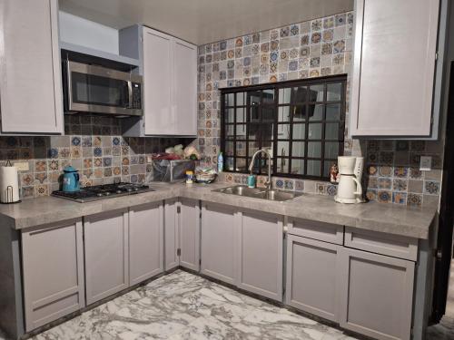 uma cozinha com armários brancos, um lavatório e uma janela em MercedesHouse em Hermosillo