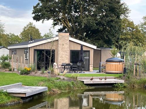 比丁赫茲的住宿－Wellness Chalet Veluwemeer，池塘旁的一座房子,里面放着鸭子