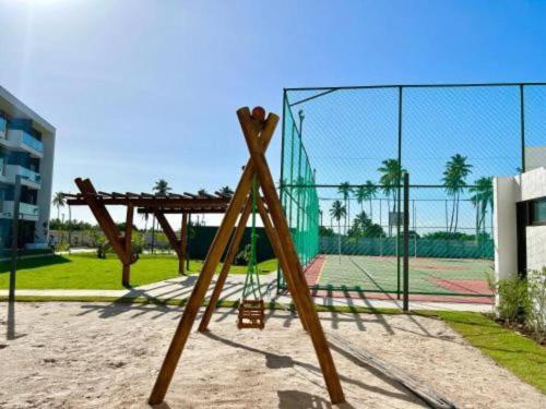 a wooden swing set in front of a tennis court at Muro Alto - Flat Completo MANA Resort in Porto De Galinhas