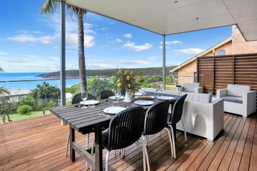 a dining table on a deck with a view of the ocean at Pambula Family Beach House in Pambula Beach