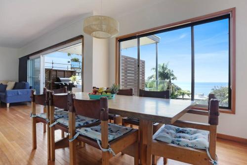 a dining room with a table and some windows at Pambula Family Beach House in Pambula Beach