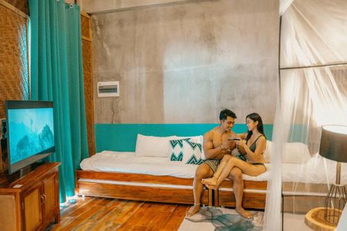 a man and woman sitting on a bed looking at their cell phones at The Verge Cebu Beachfront King Bed Pool Villa - 12 Minutes to Kawasan Falls Canyoneering in Badian