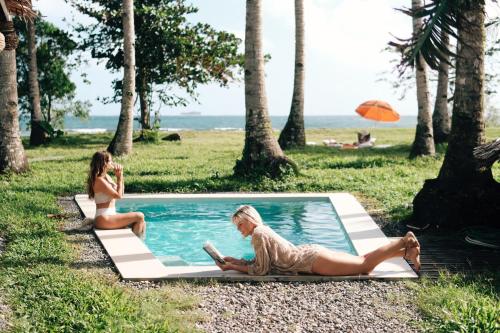 two women sitting around a swimming pool next to a beach at Punta Punta Surf Retreat in General Luna