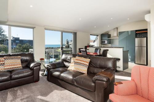 a living room with leather furniture and a kitchen at Longbeach Ocean Paradise in Mount Maunganui