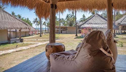 a chair on a porch with a straw roof at Bleu MATHIS Gili Asahan in Gili Asahan