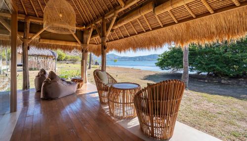 a porch with chairs and tables and a straw umbrella at Bleu MATHIS Gili Asahan in Gili Asahan