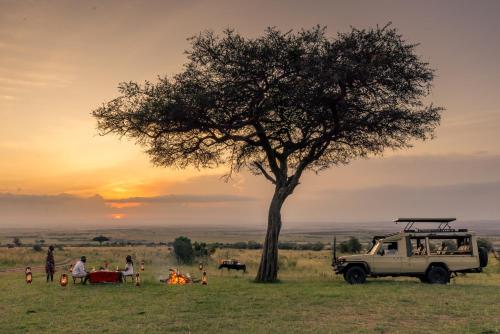 a group of people sitting in a field next to a tree at Sentrim Mara Lodge in Ololaimutiek