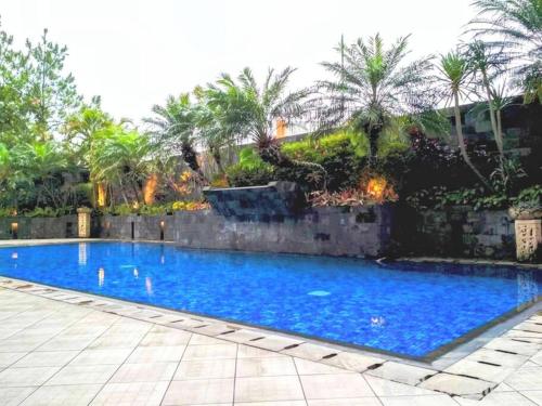 a large blue swimming pool with a stone wall and palm trees at Cottonwood Japandi Apartment at Majesty 509 in Bandung