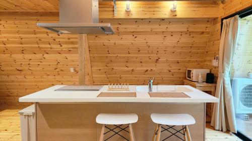 a kitchen with wooden walls and a counter with stools at Kitagi Cabin in Hakuba