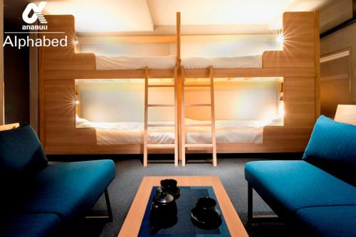 高松市にあるALPHABED INN Takamatsuekimaeの二段ベッド1組、椅子2脚、テーブルが備わる客室です。