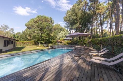 - une piscine avec des chaises et un parasol sur une terrasse en bois dans l'établissement La Kayola, à Soorts-Hossegor