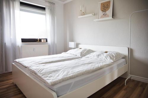 a white bed in a white bedroom with a window at DG-Wohnung mit sonnigem Balkon in Marburg an der Lahn