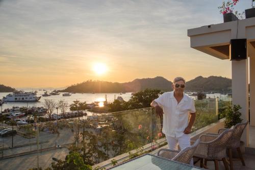 a man standing on a balcony with a view of a harbor at DEJAVU 2.0 HOTEL BAJO KOMODO in Labuan Bajo