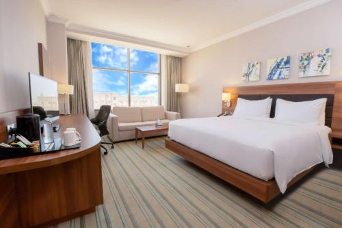 Habitación de hotel con cama blanca grande y escritorio. en Hilton Garden Inn Al Jubail en Al Jubail