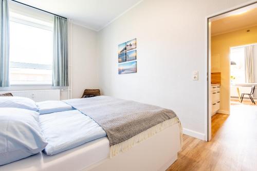 a white bedroom with a bed and a large window at Steger-Hüs Wohnung 19 in Rantum