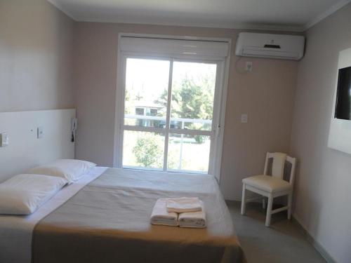 um quarto com uma cama, uma cadeira e uma janela em Hotel Jardim do Mar em Torres
