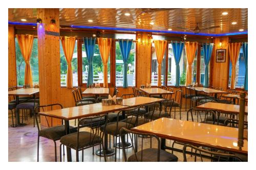 un ristorante con tavoli e sedie in legno e finestre di Shivalik River Retreat ad Almora