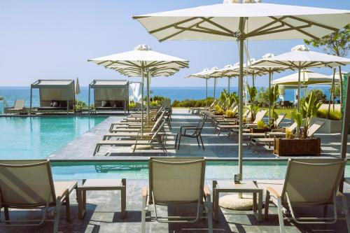 una piscina con mesas, sillas y sombrillas en Anasa Luxury Resort, en Elaiokhórion