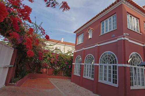 a red building with white windows and red flowers at Vila Olivença in Costa da Caparica