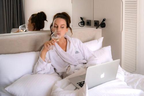 a woman sitting in bed with a glass of wine and a laptop at Bayview Hills Luxury Residences in Tivat