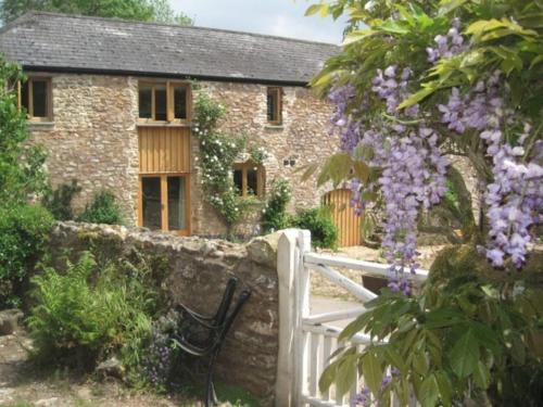 a stone cottage with a white fence and purple flowers at Luggs Barn - Beautiful Devon Hideaway in Hemyock