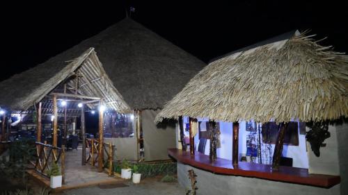 dois pequenos edifícios com telhados de palha à noite em Tausa Tsavo Eco Lodge em Voi