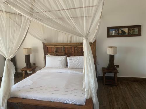 1 dormitorio con cama con dosel, sábanas y almohadas blancas en Zi Loft Beach Cottage, en Matemwe