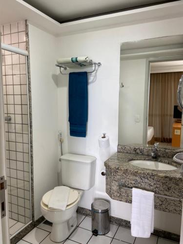 a bathroom with a toilet and a sink and a mirror at Praia do Canto Apart Hotel in Vitória