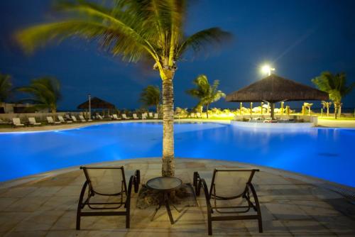 una mesa y sillas frente a una piscina por la noche en HOTEL DOM PEDRO LAGUNA, en Aquiraz