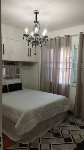 um quarto com uma cama branca e um lustre em Aconchegante apt c/ garagem em Serra Negra