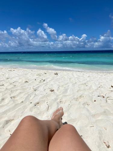 a woman sitting on a beach with her legs in the sand at Beach Veli in Ukulhas