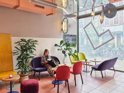 una donna seduta su un divano in una stanza con sedie e tavoli di CityHub Rotterdam a Rotterdam