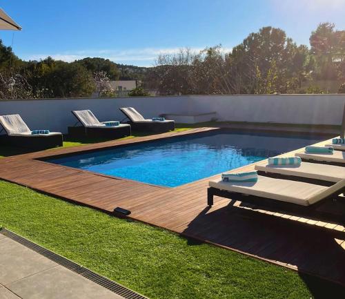 una piscina con sillas y una terraza de madera en Tranquil and spacious 5 bedroom family villa, en Sant Pere de Ribes
