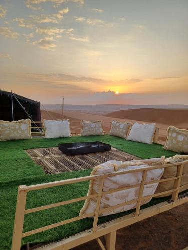 Badīyah的住宿－Sunrise Desert Local Private Camp，沙漠中的一张床铺,背景是日落