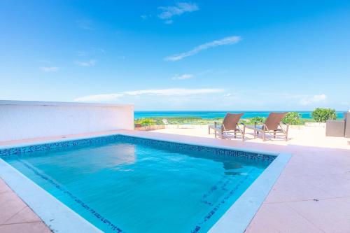 einen Pool mit Stühlen und das Meer im Hintergrund in der Unterkunft Pristine Bay 1303 villa in Roatán